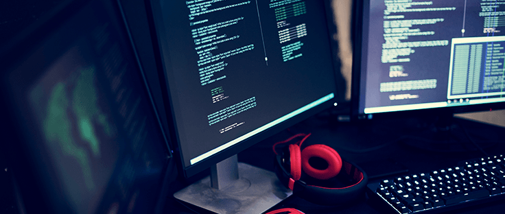Computer monitors with code on screen and red headphones and a keyboard in front